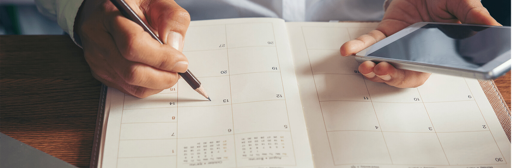 Hands marking a date in a calendar while holding a phont